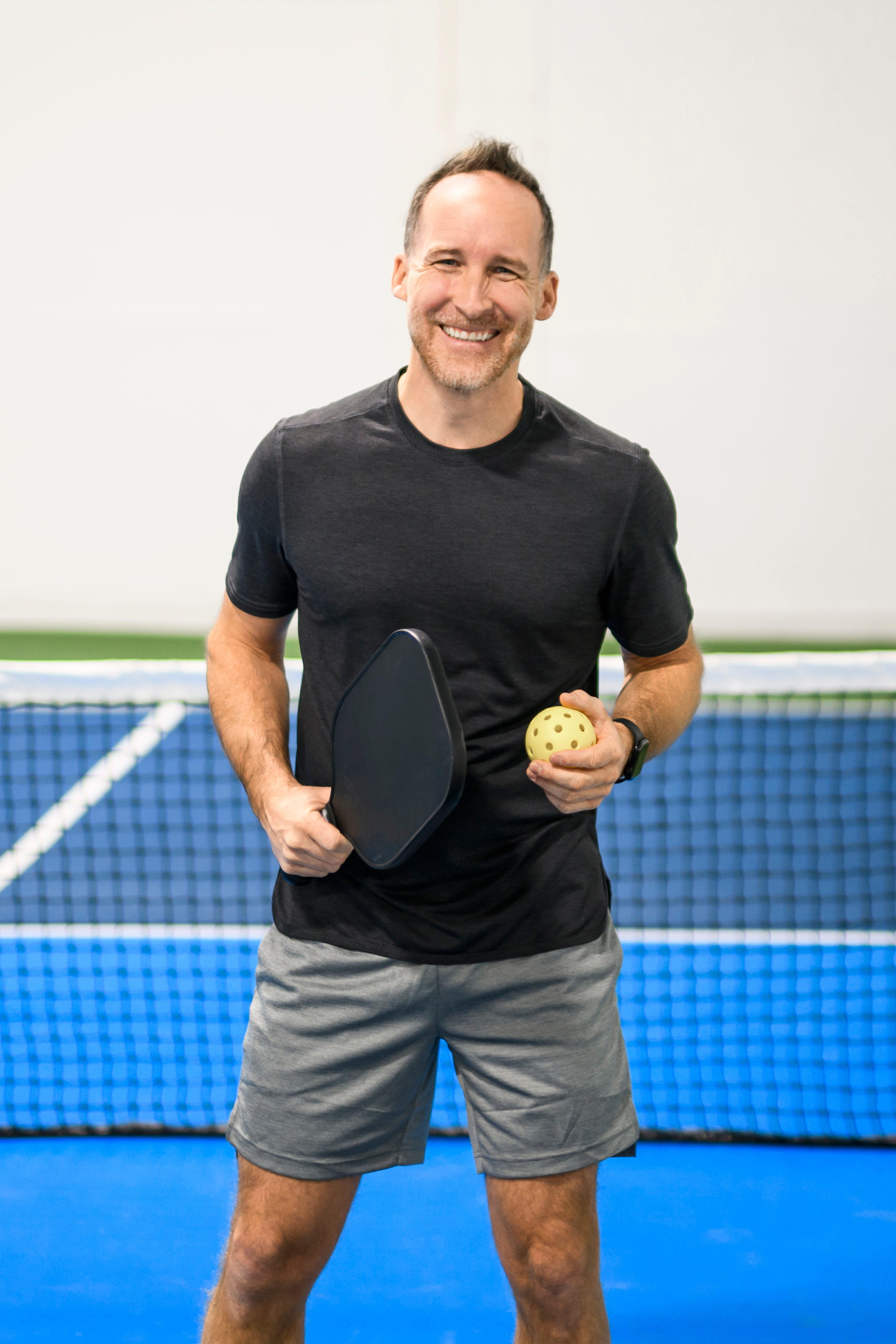 Portrait of pickleball coach Steven Hammer smiling with a paddle and ball on a blue indoor court