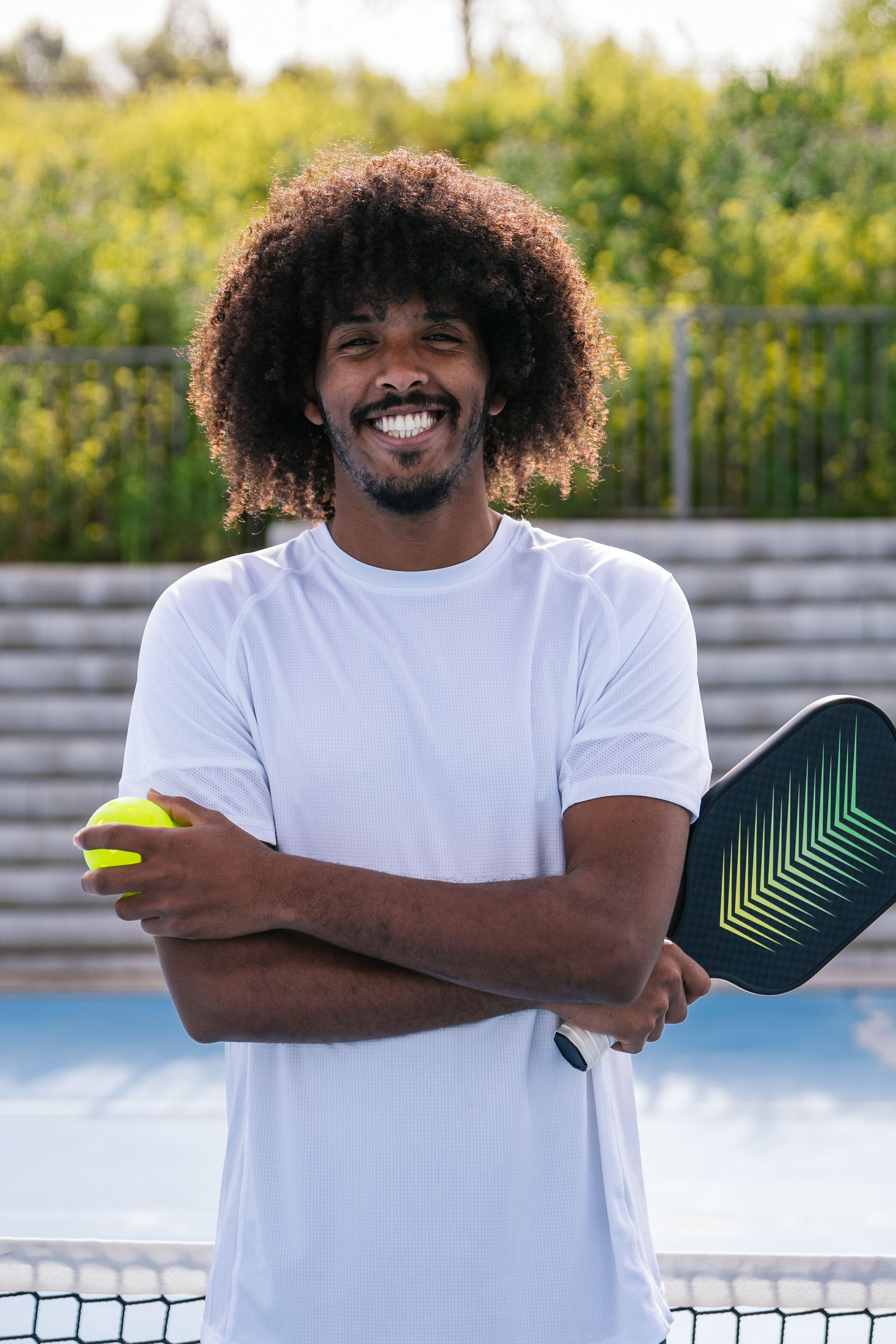 Portrait of pickleball coach Ben Sosville with arms crossed holding a paddle and ball on an outdoor court