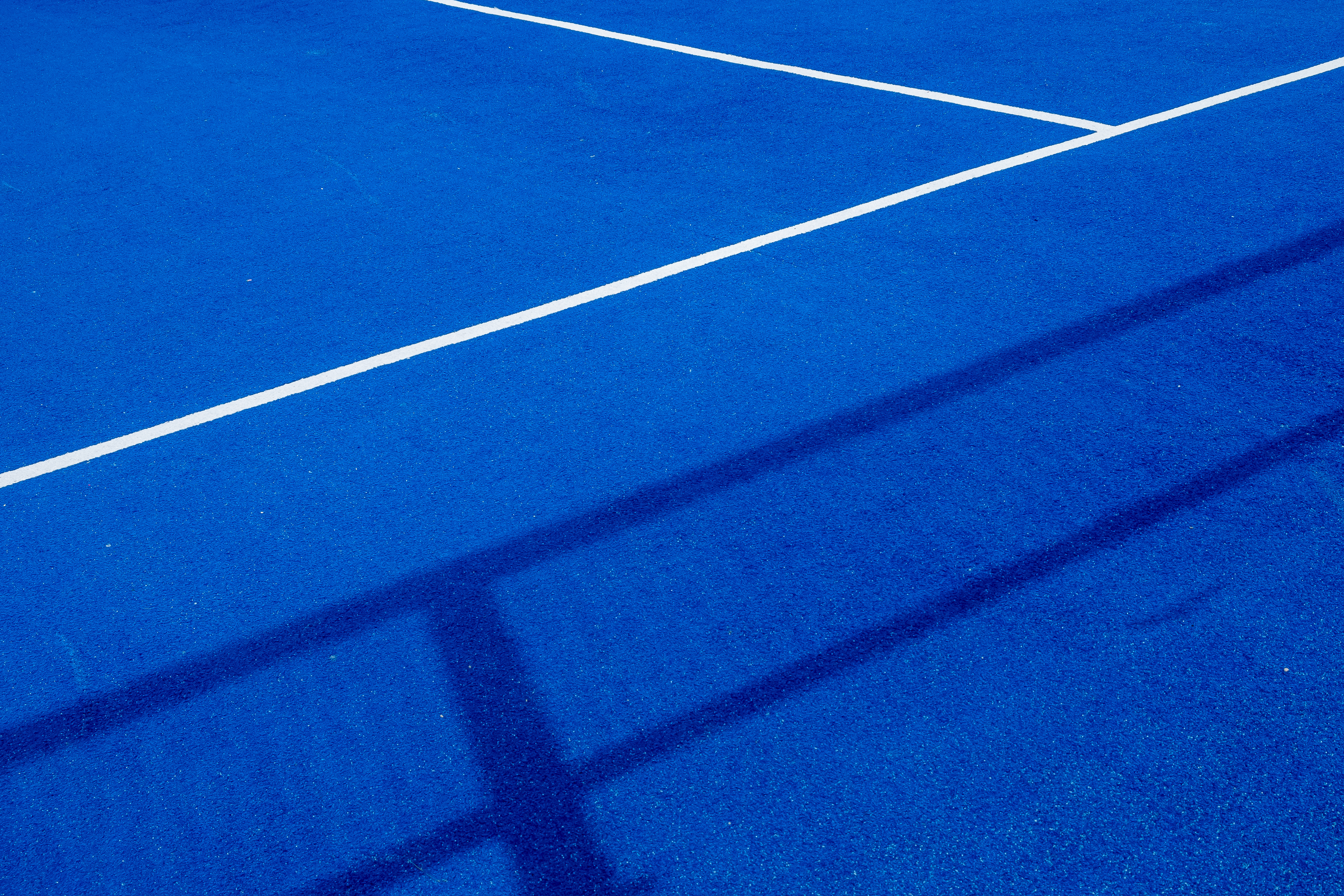 Close-up view of a blue indoor pickleball court surface with white lines and net shadows