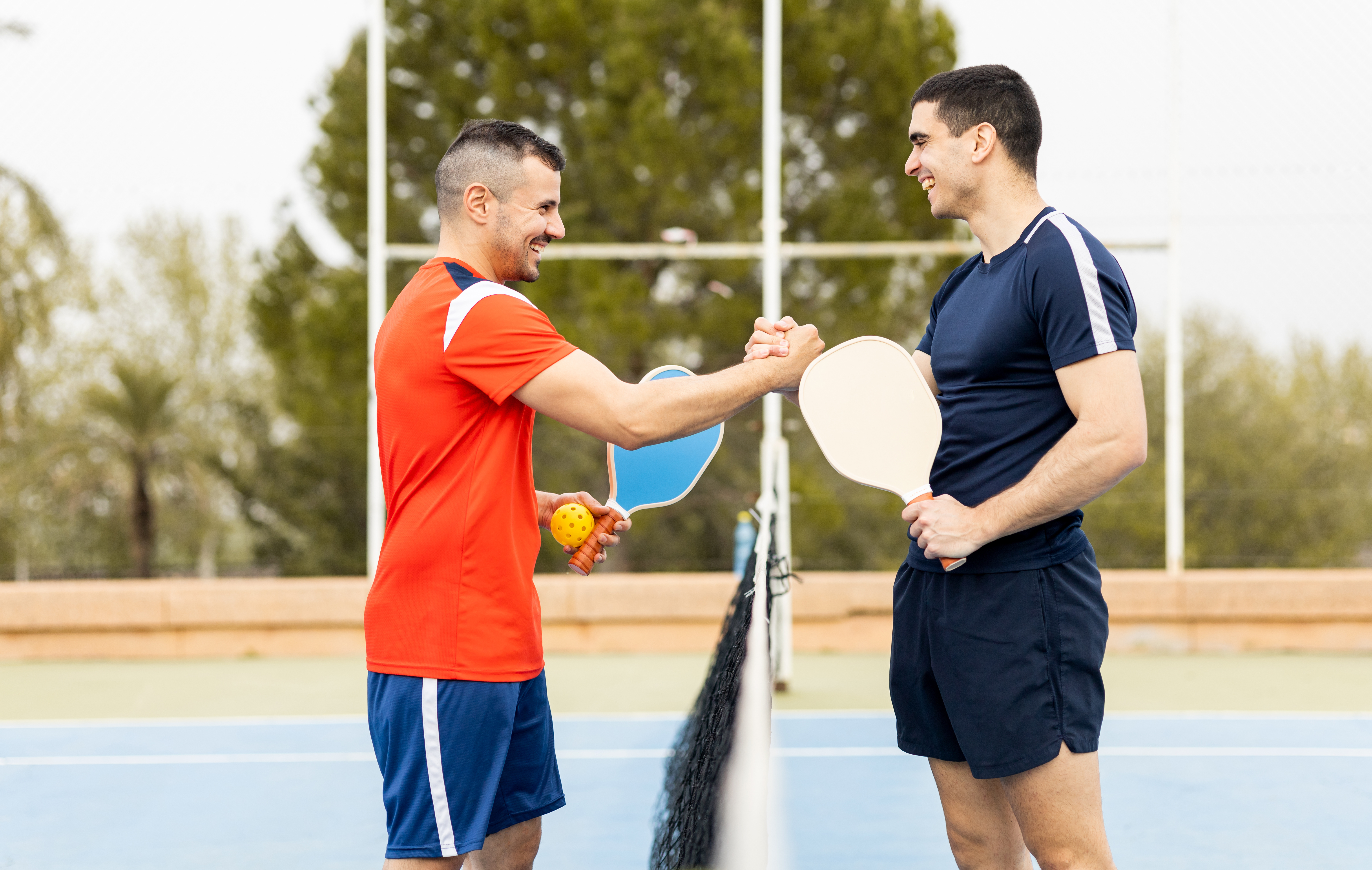 Two men smiling and shaking hands over the net after a pickleball game during a private event